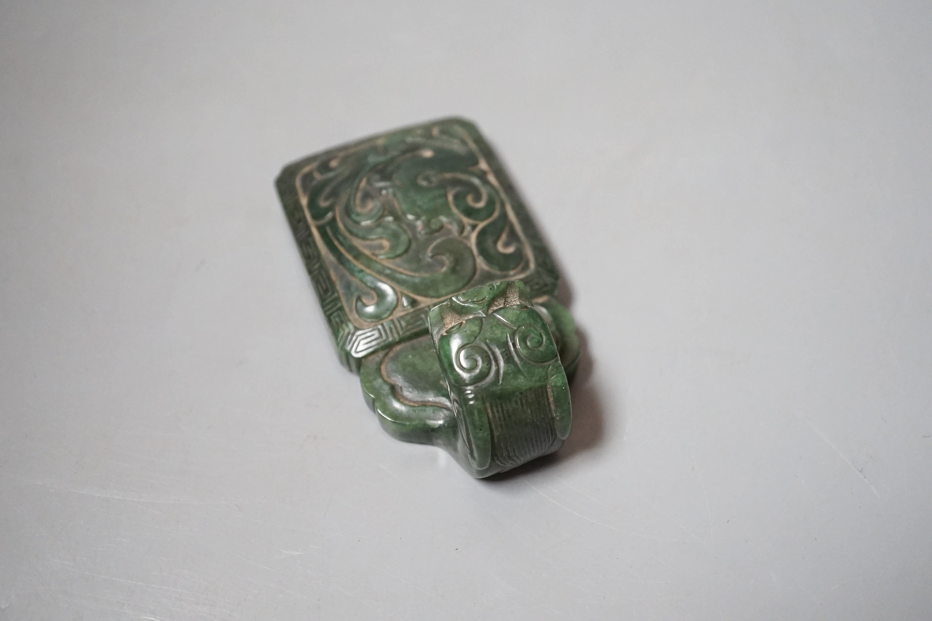 A Chinese spinach green jade belt hook, 19th century, in archaistic style, carved in relief with a chi-dragon, with a dragon head handle, 9cm